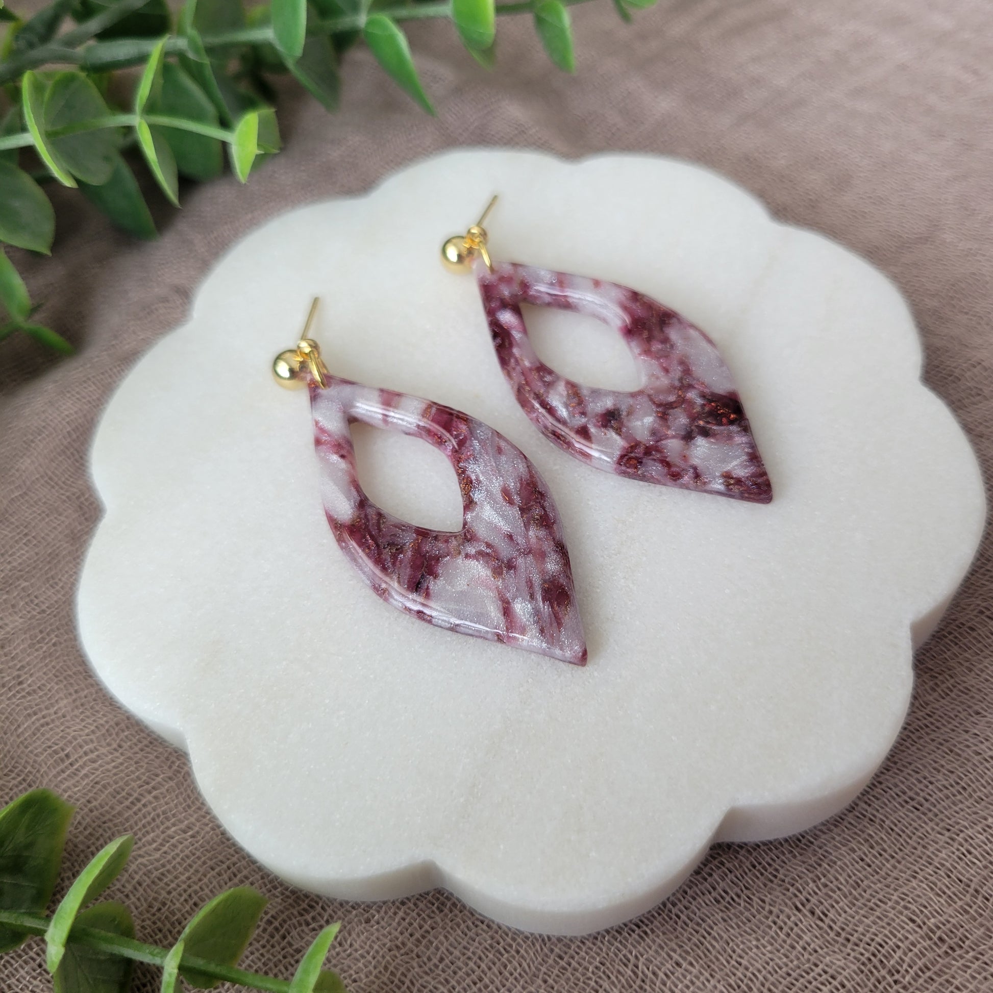 Left side view of a pair of maroon, pearl earrings displayed on a white round scalloped tray.