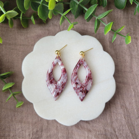 Top view of a pair of maroon, pearl earrings displayed on a white round scalloped tray.