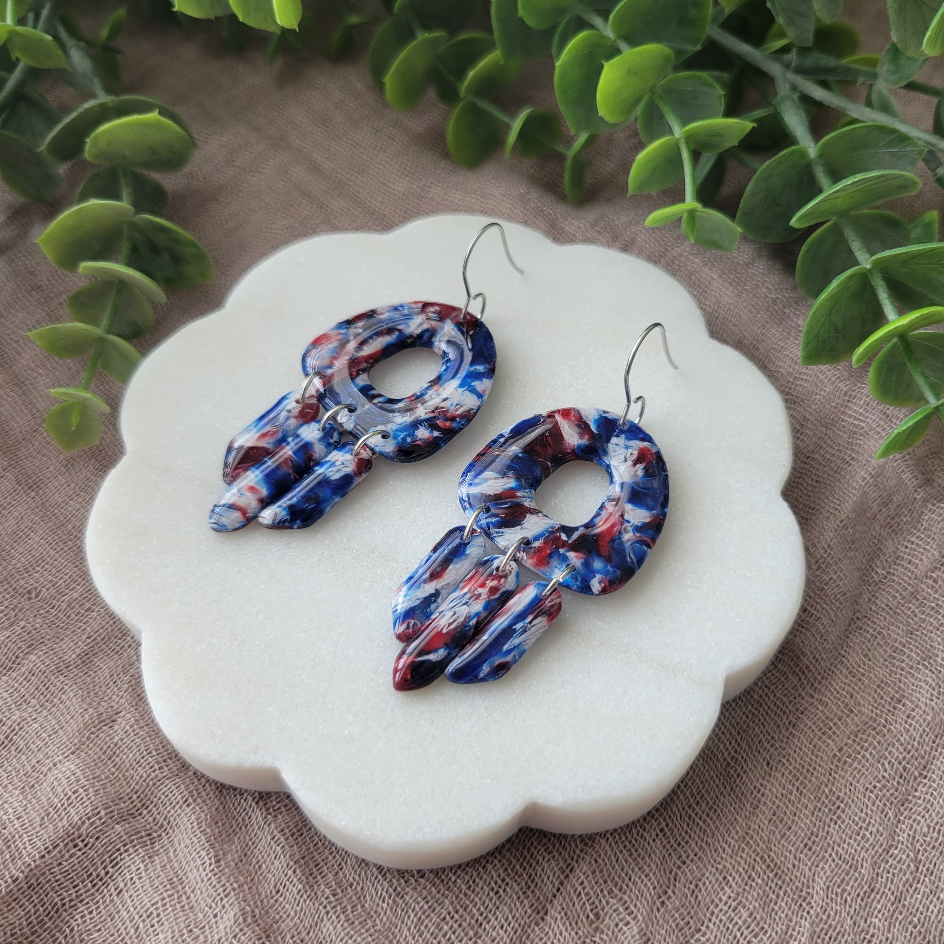 Right side view of a pair of red, white, blue marble earrings displayed on a white round scalloped tray.