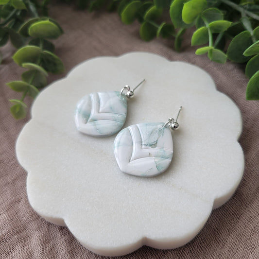 Right side view of a pair of  tiffany blue, white marble embossed round tear drop shaped earrings displayed on a white round scalloped tray.