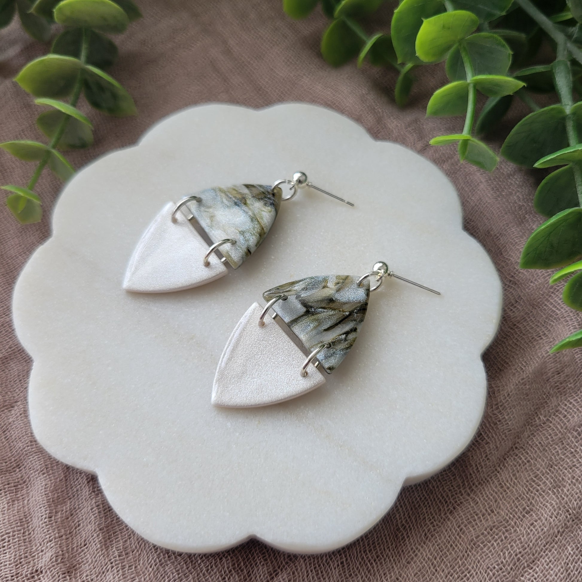 Right side view of a pair of moss and pearl colored earrings displayed on a white round scalloped tray.