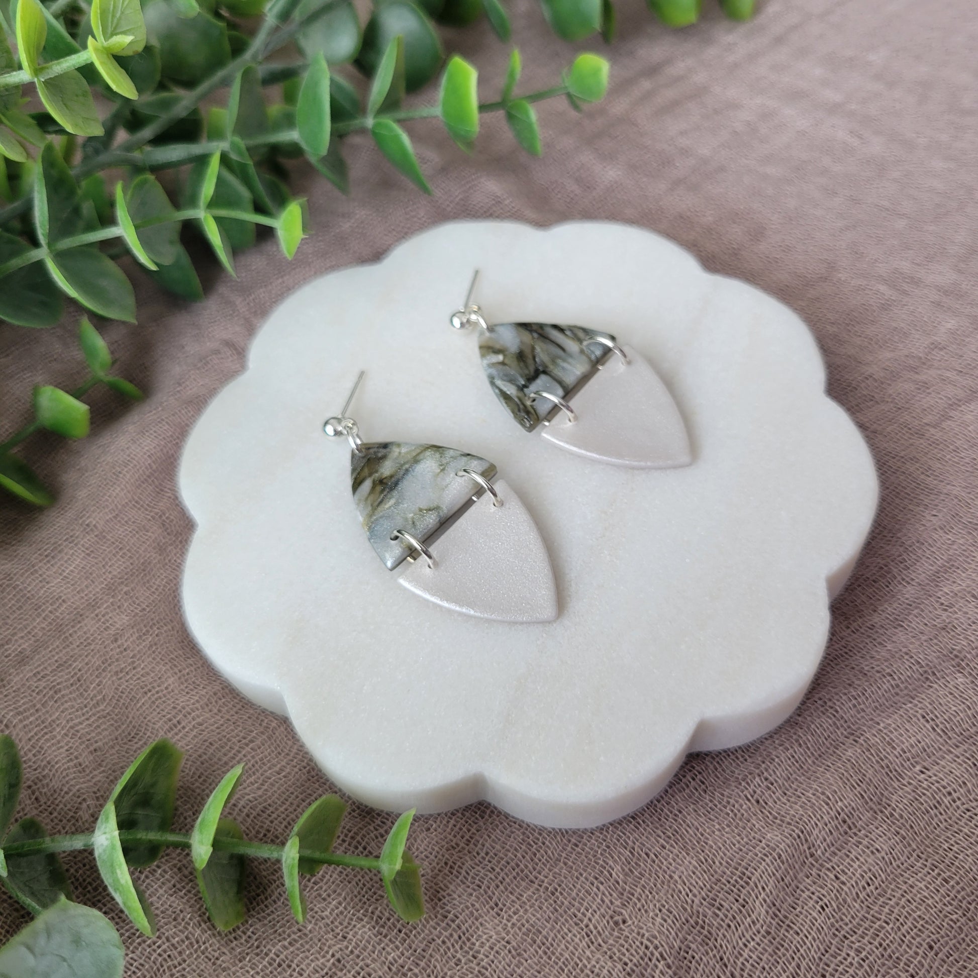 Left side view of a pair of moss and pearl colored earrings displayed on a white round scalloped tray.