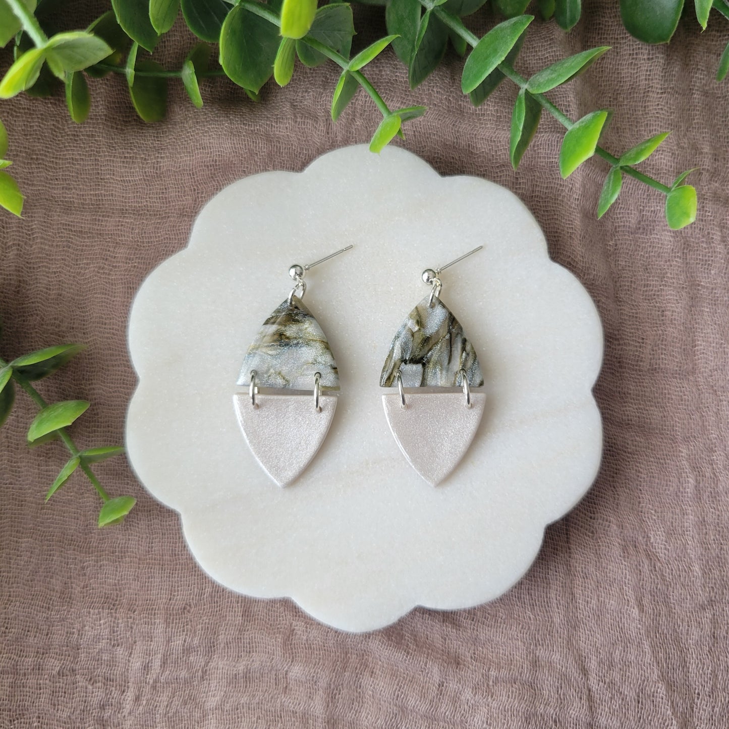 Top view of a pair of moss and pearl colored earrings displayed on a white round scalloped tray.