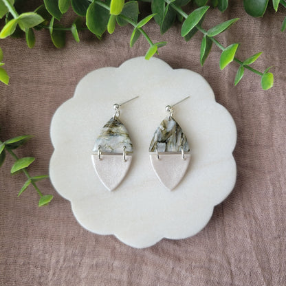 Top view of a pair of moss and pearl colored earrings displayed on a white round scalloped tray.