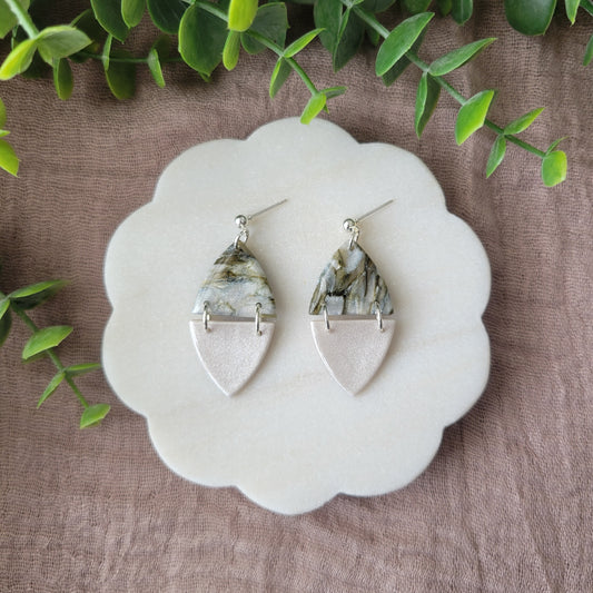 Top view of a pair of moss and pearl colored earrings displayed on a white round scalloped tray.