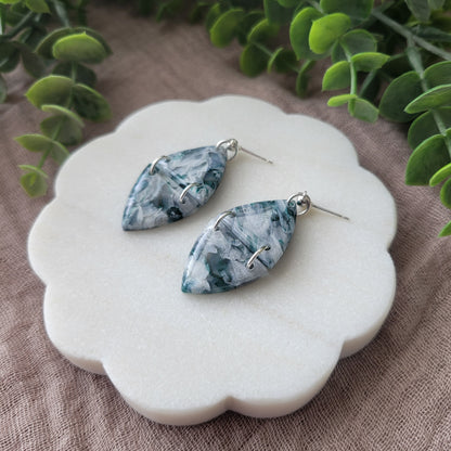 Right side view of a pair of green, white, silver marble earrings displayed on a white round scalloped tray.