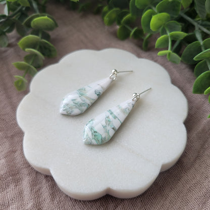 Right side view of a pair of tiffany blue, white marble elongated tear drop shaped earrings displayed on a white scalloped tray.