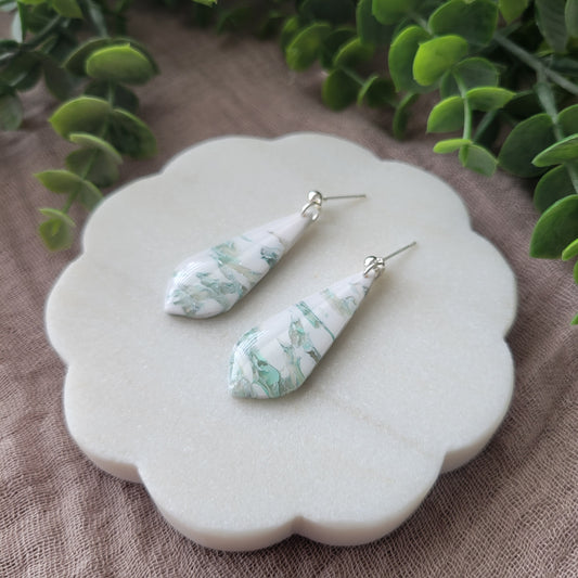 Right side view of a pair of tiffany blue, white marble elongated tear drop shaped earrings displayed on a white scalloped tray.