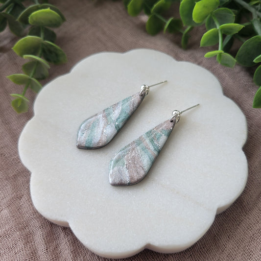 Right side view of a pair of shimmering pastel elongated tear drop shaped earrings displayed on a white round scalloped tray.