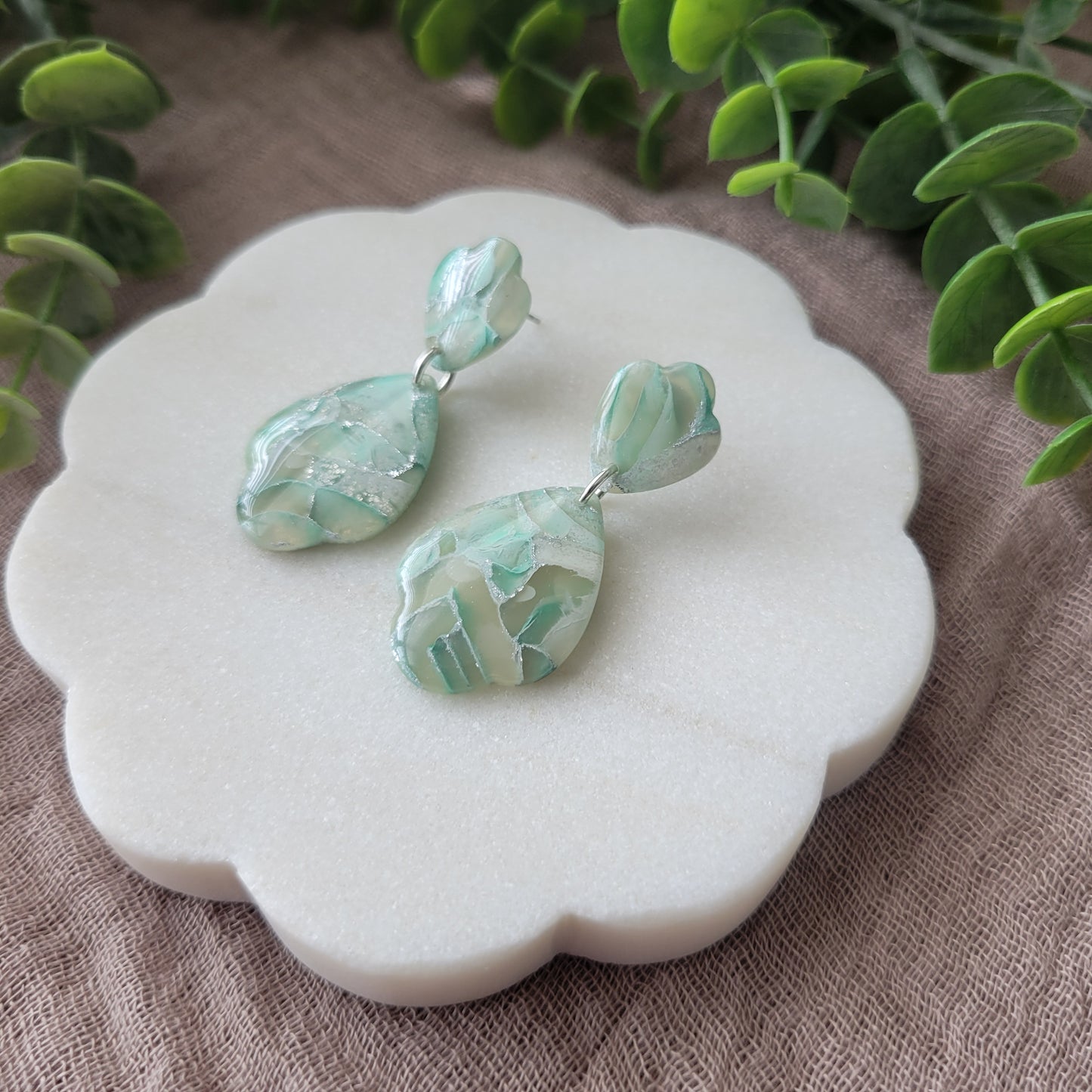 Right side view of a pair of mint green marble scalloped teardrop shaped earrings displayed on a white round scalloped tray.