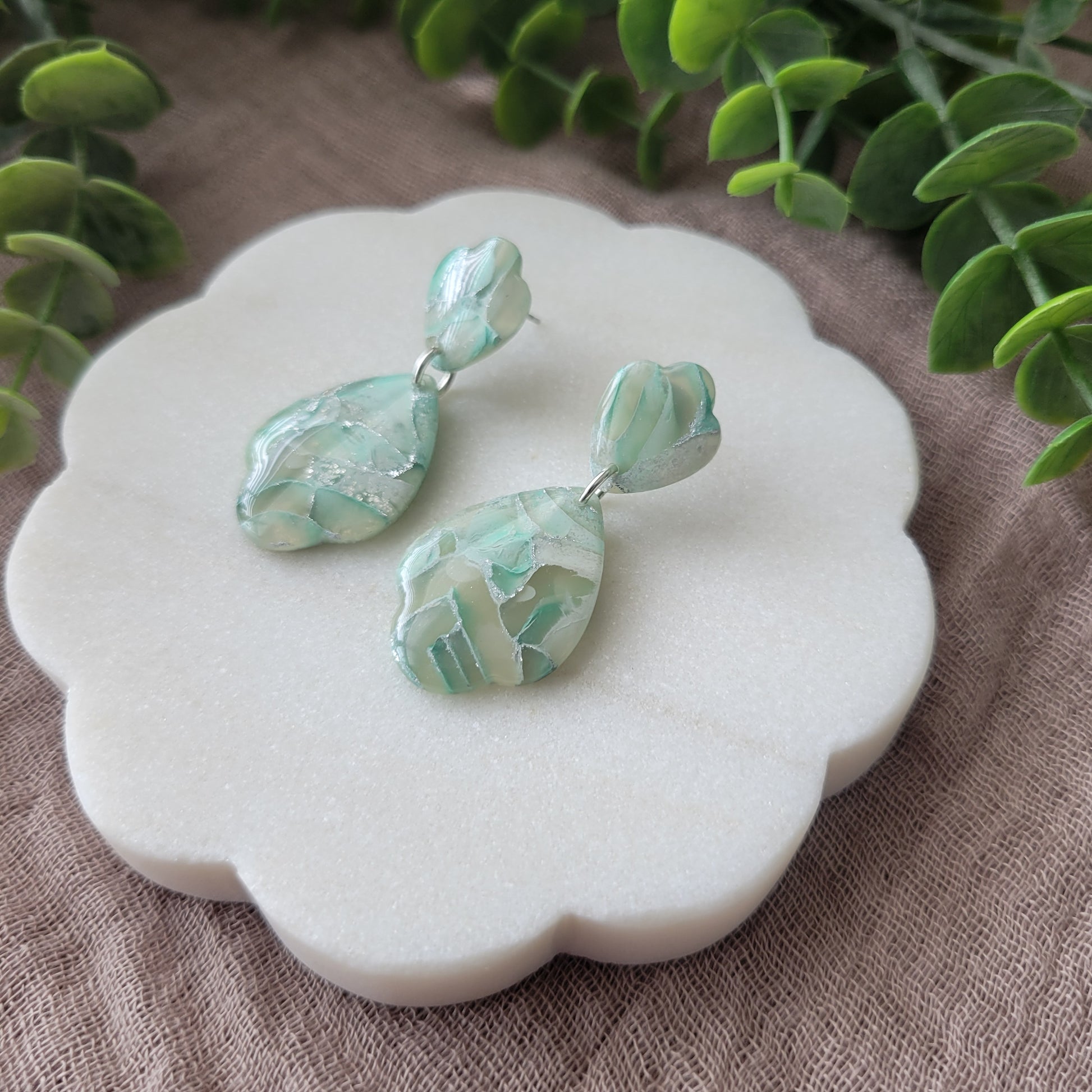 Right side view of a pair of mint green marble scalloped teardrop shaped earrings displayed on a white round scalloped tray.
