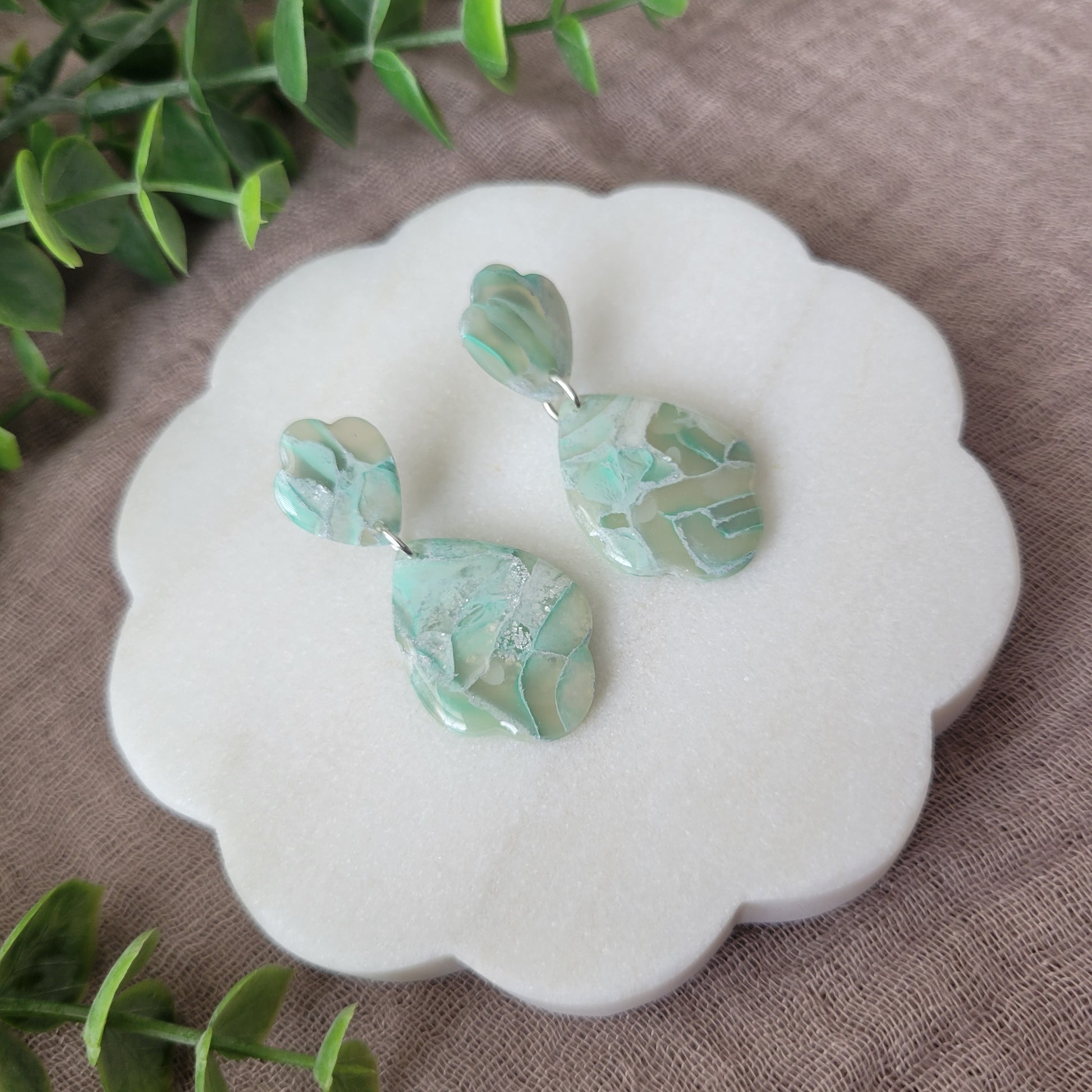 Left side view of a pair of mint green marble scalloped teardrop shaped earrings displayed on a white round scalloped tray.