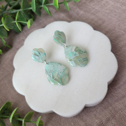 Left side view of a pair of mint green marble scalloped teardrop shaped earrings displayed on a white round scalloped tray.