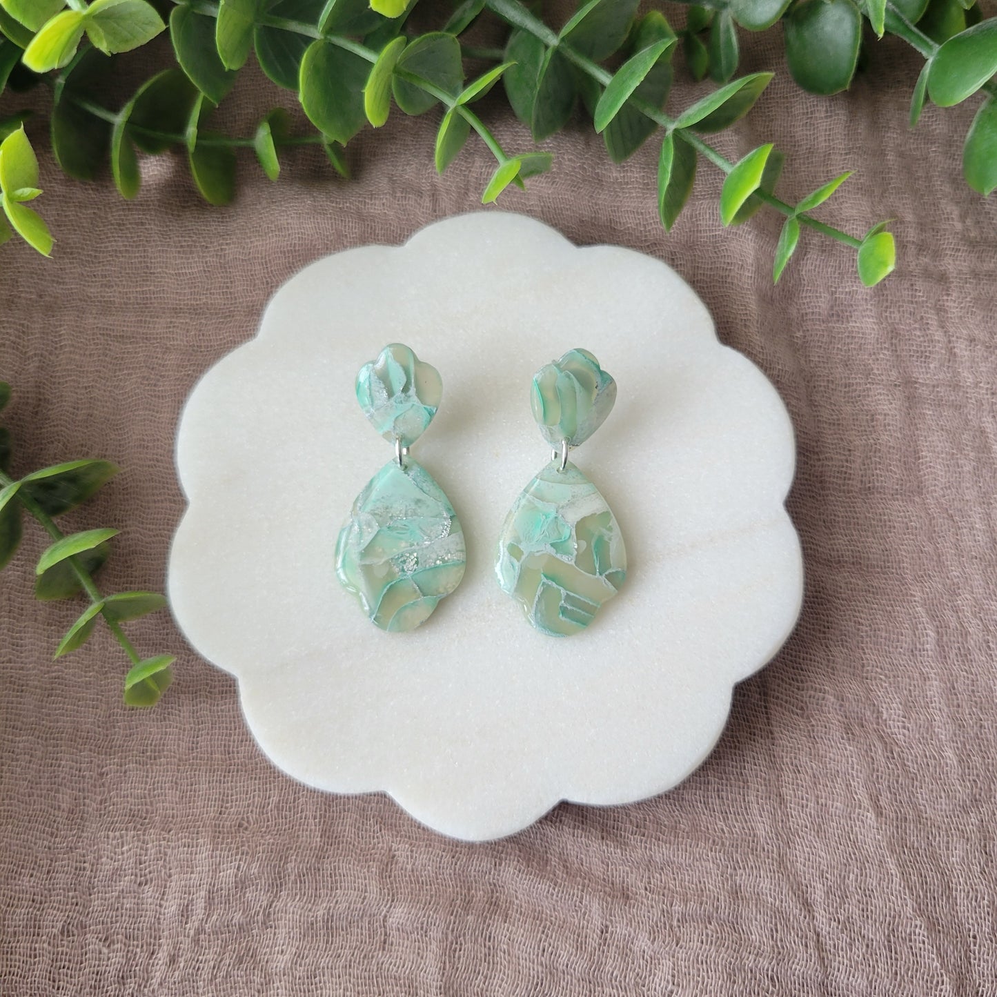 Top view of a pair of mint green marble scalloped teardrop shaped earrings displayed on a white round scalloped tray.