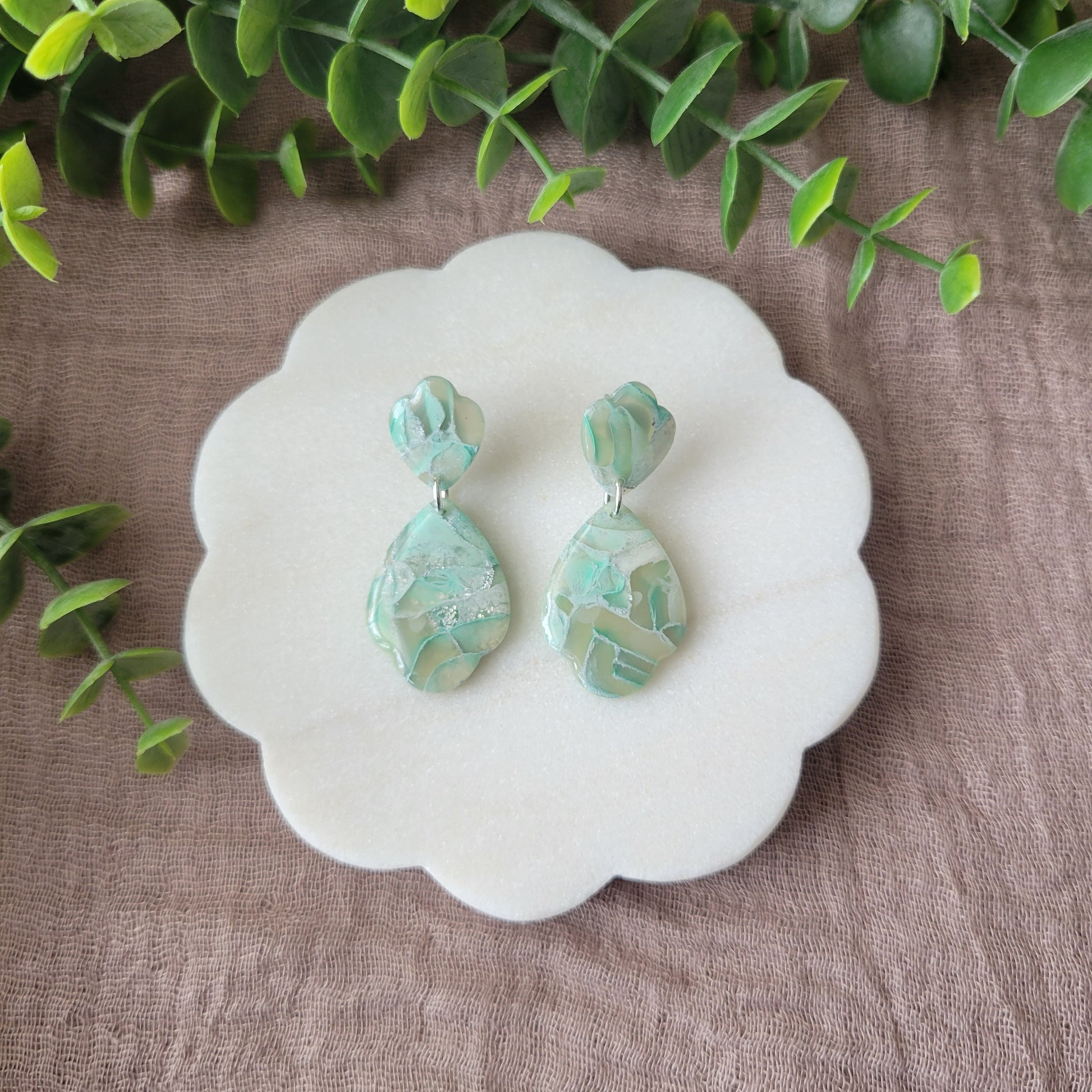 Top view of a pair of mint green marble scalloped teardrop shaped earrings displayed on a white round scalloped tray.