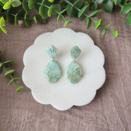 Top view of a pair of mint green marble scalloped teardrop shaped earrings displayed on a white round scalloped tray.