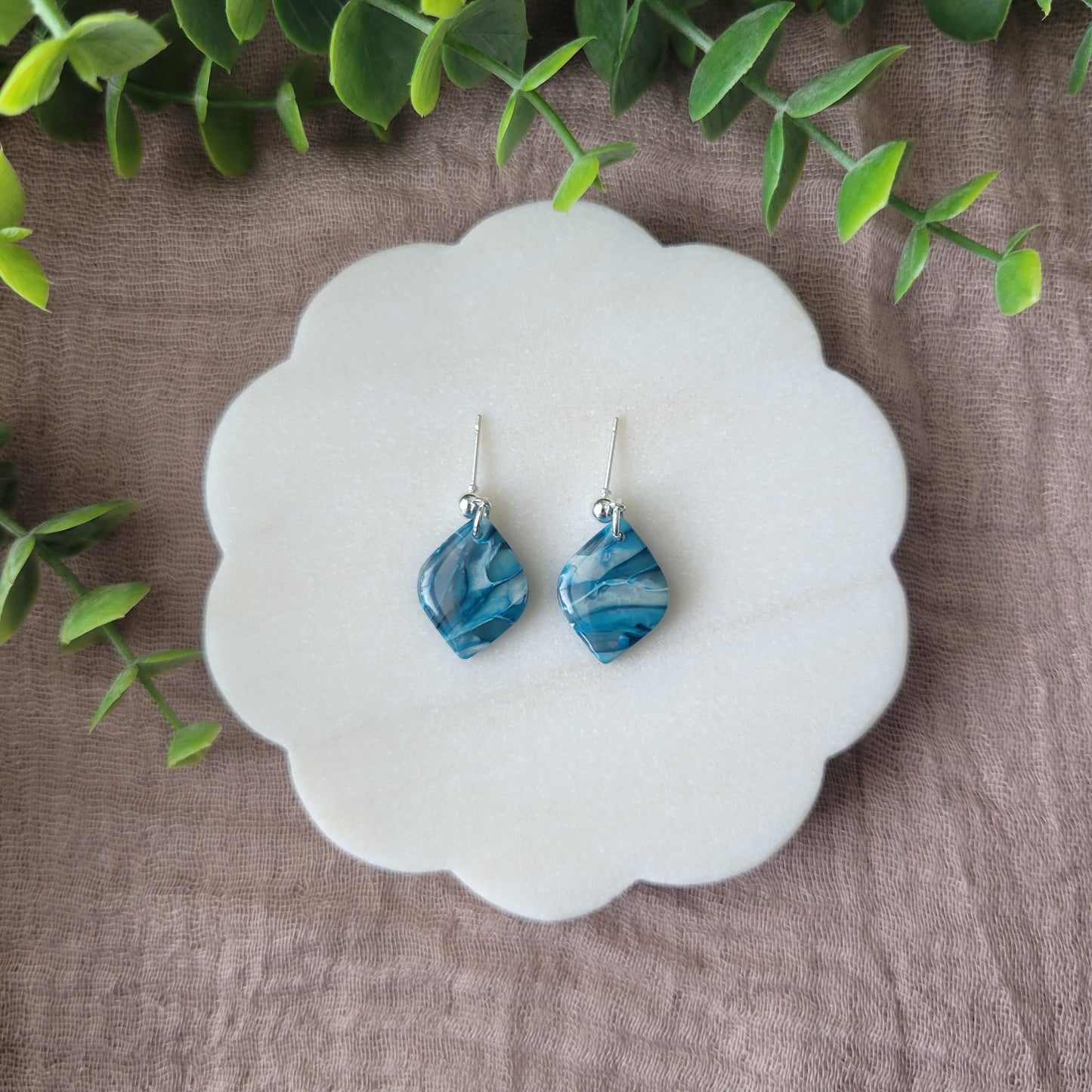 Top view of a pair of blue marble diamond shaped earrings displayed on a white round scalloped tray.