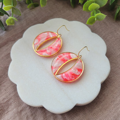 Right side view of a pair of round polymer clay earrings in the color bright pink and pearl with gold trim on a white scalloped tray.