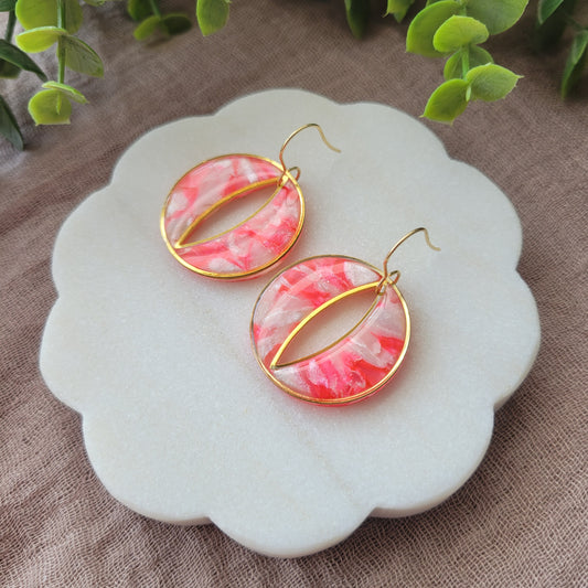 Right side view of a pair of round polymer clay earrings in the color bright pink and pearl with gold trim on a white scalloped tray.