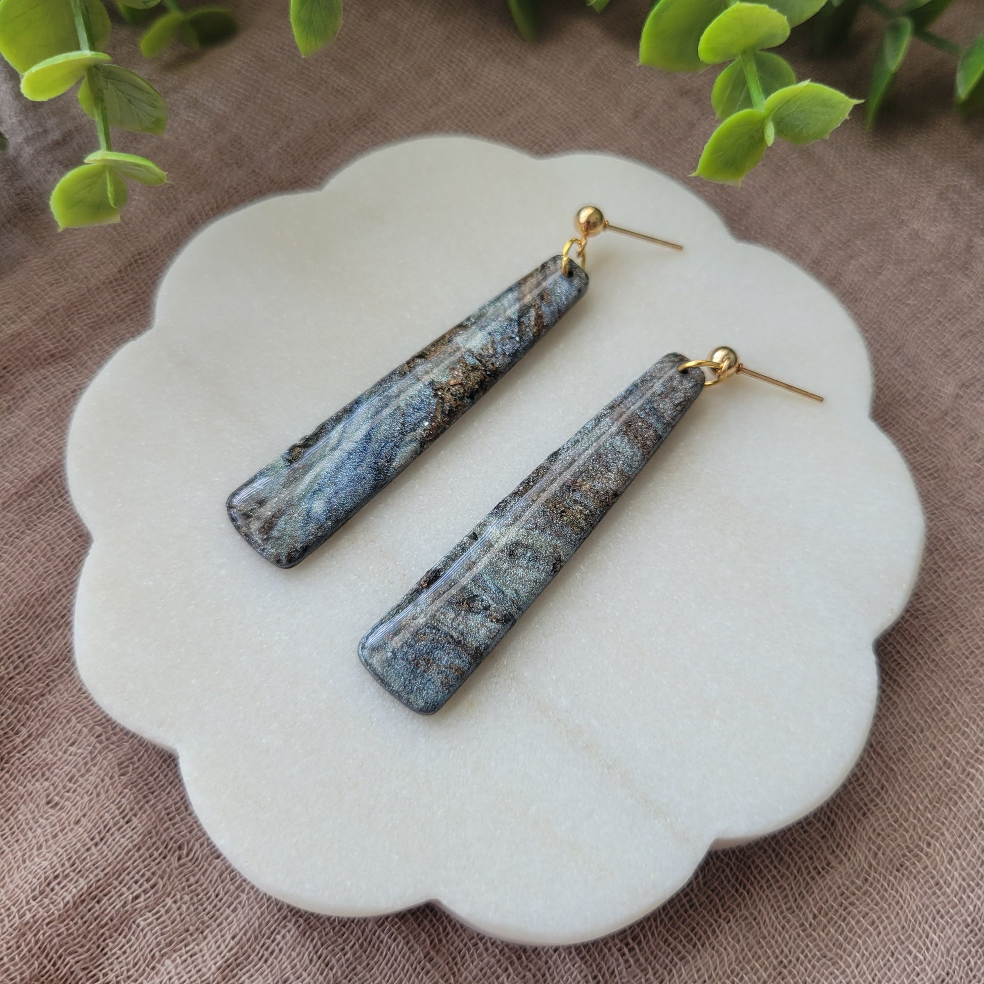 Right side view of a pair of gray, brown pillar shaped earrings displayed on a white round scalloped tray.