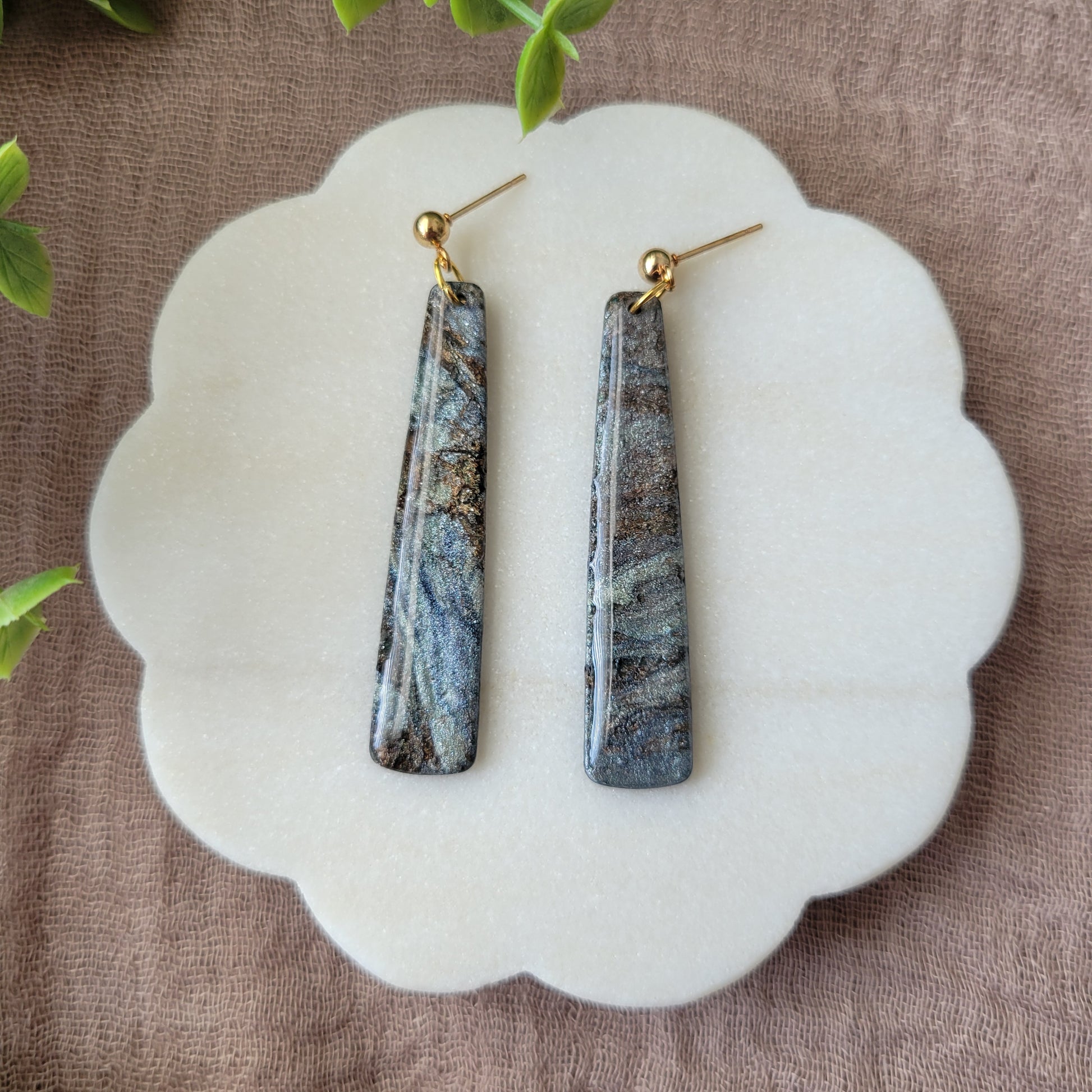 Top view of a pair of gray, brown pillar shaped earrings displayed on a white round scalloped tray.