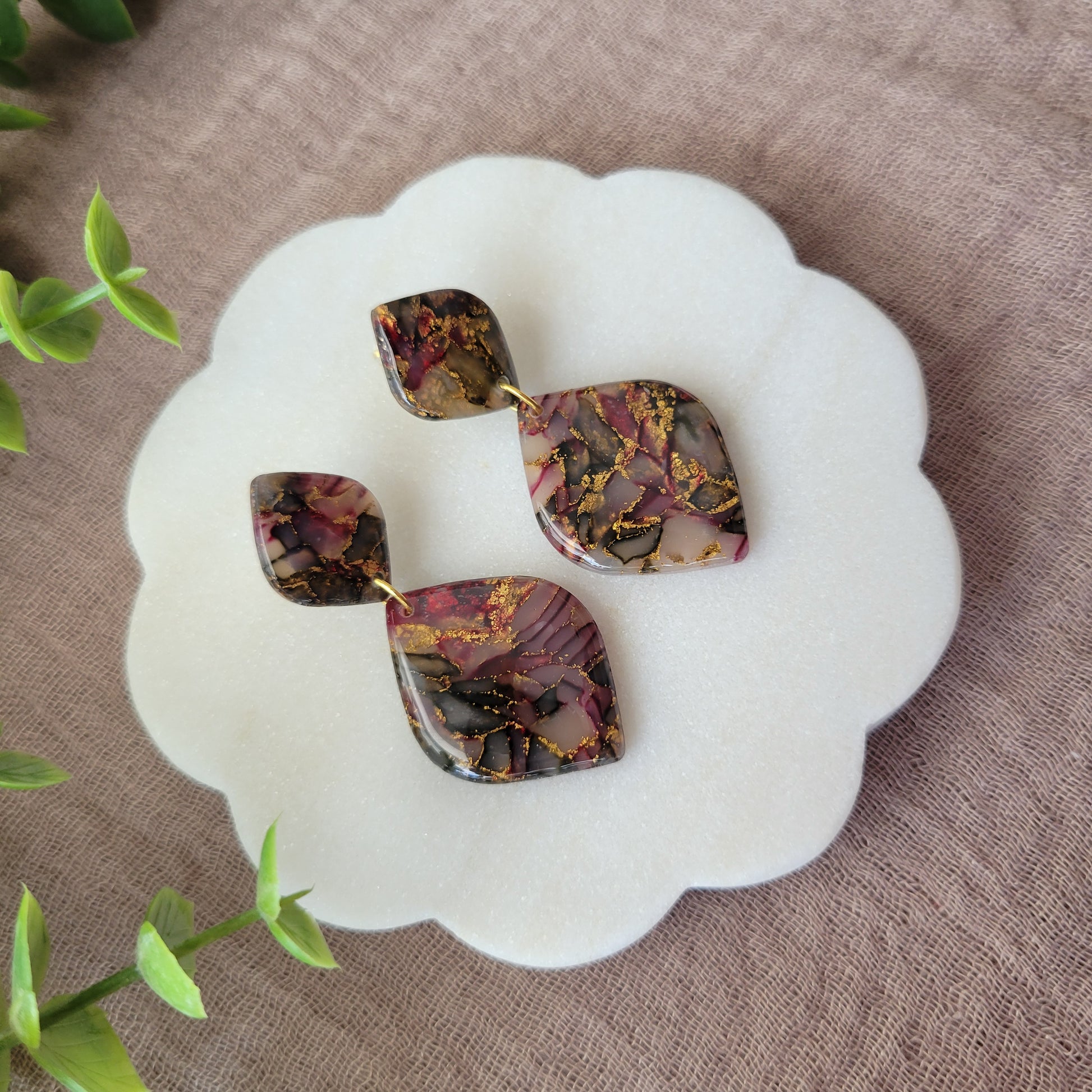 Left side view of a pair of moss, cherry, gold earrings displayed on a white round scalloped tray.