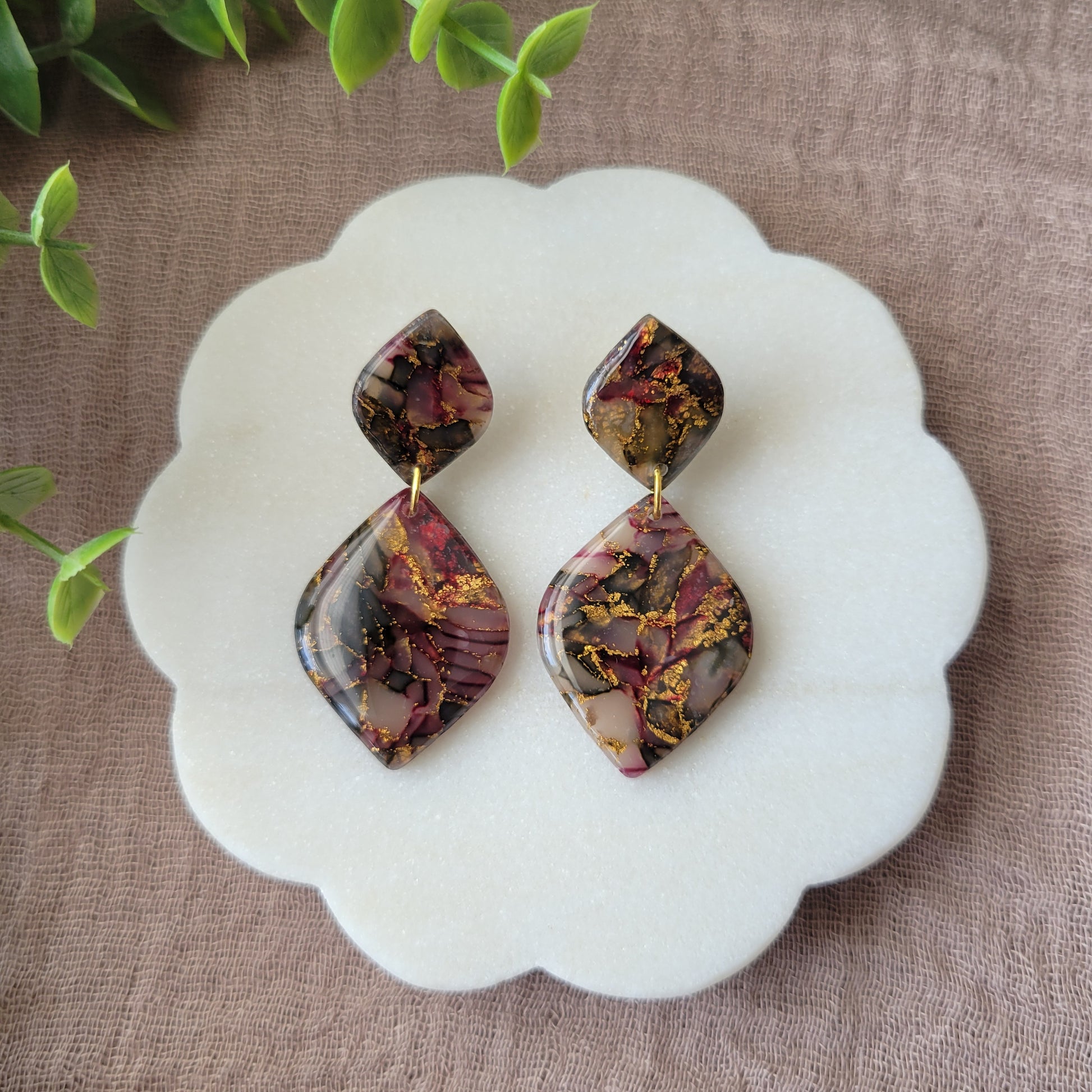 Top view of a pair of moss, cherry, gold earrings displayed on a white round scalloped tray.
