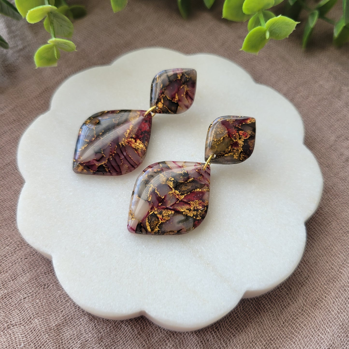 Right side view of a pair of moss, cherry, gold earrings displayed on a white round scalloped tray.