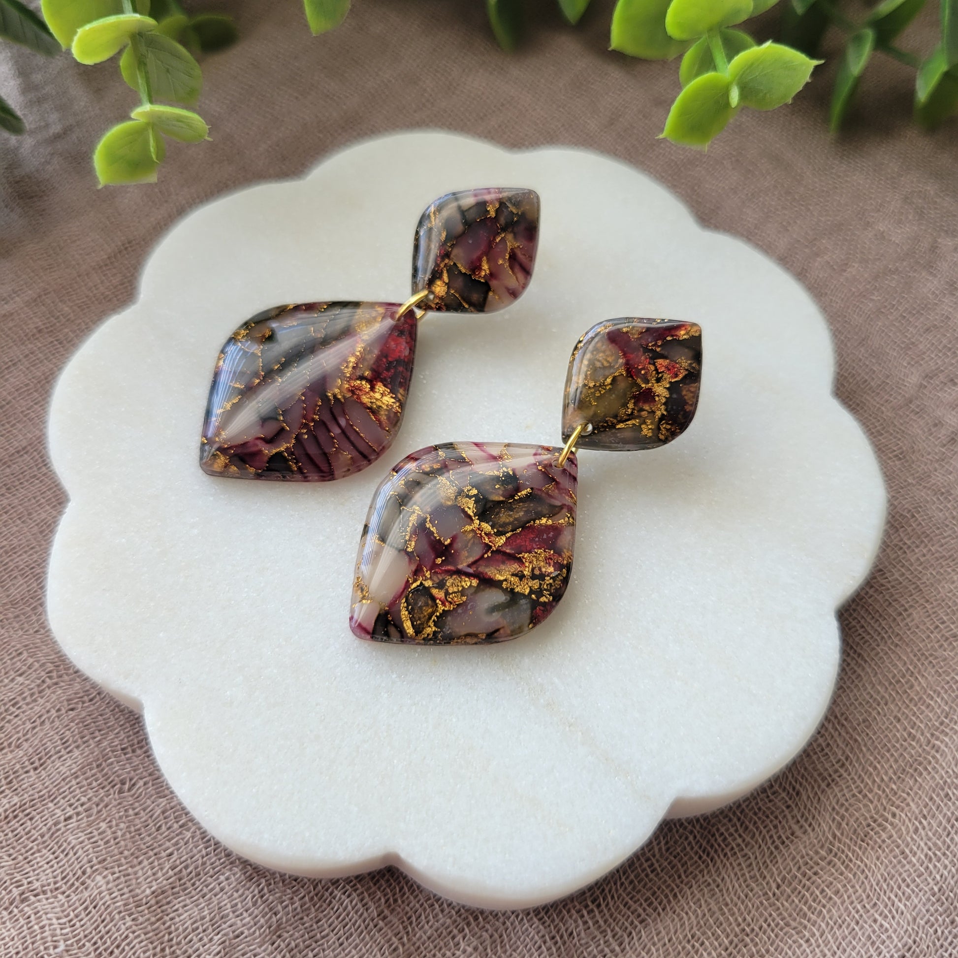 Right side view of a pair of moss, cherry, gold earrings displayed on a white round scalloped tray.