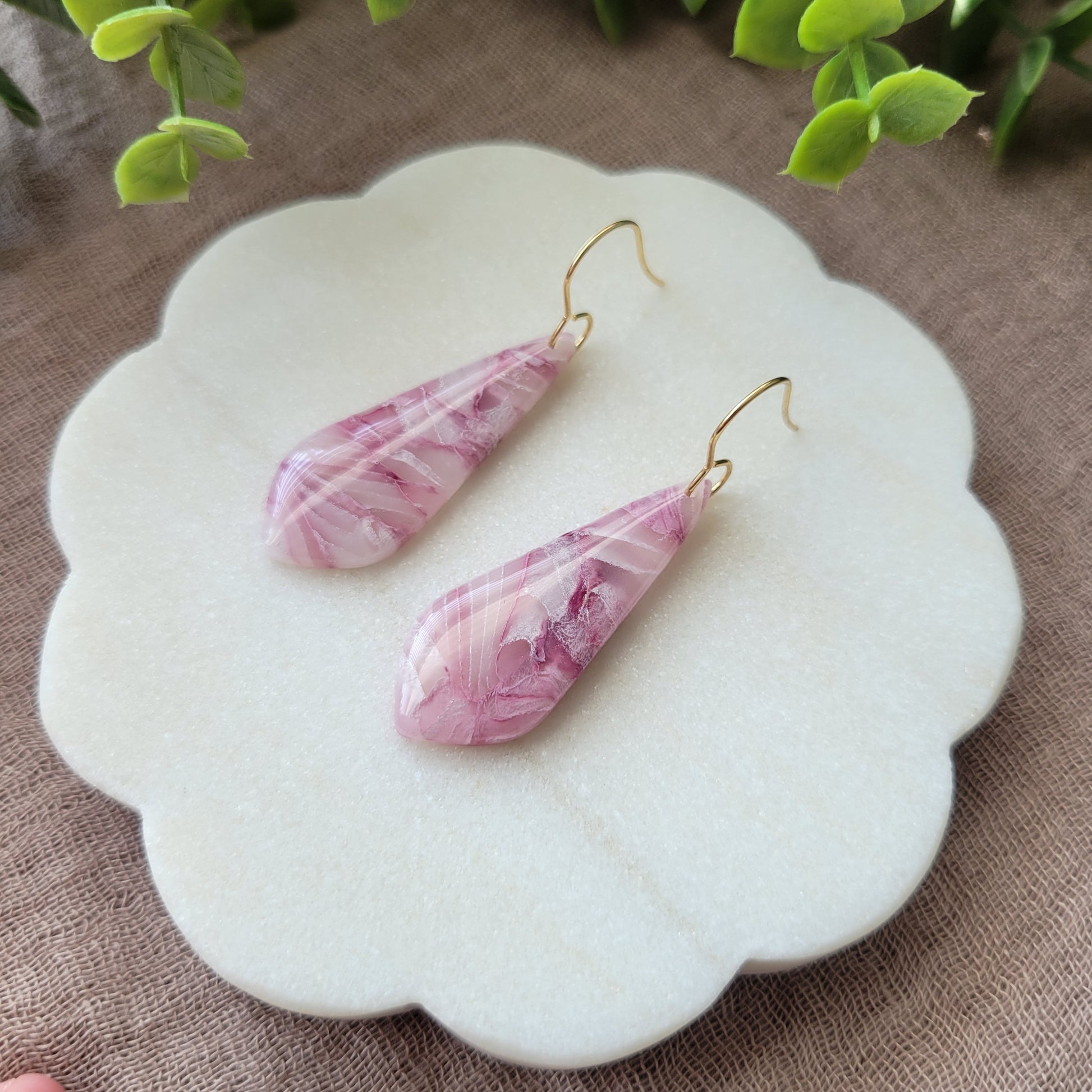 Right side view of a pair of pink marble long teardrop shaped earrings displayed on a white round scalloped tray.