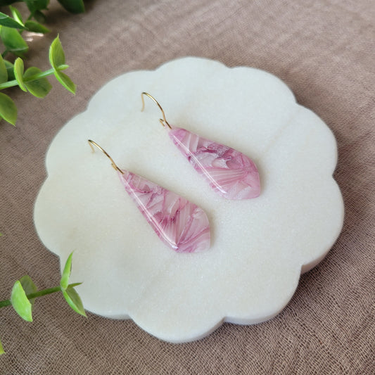 Left side view of a pair of pink marble long teardrop shaped earrings displayed on a white round scalloped tray.