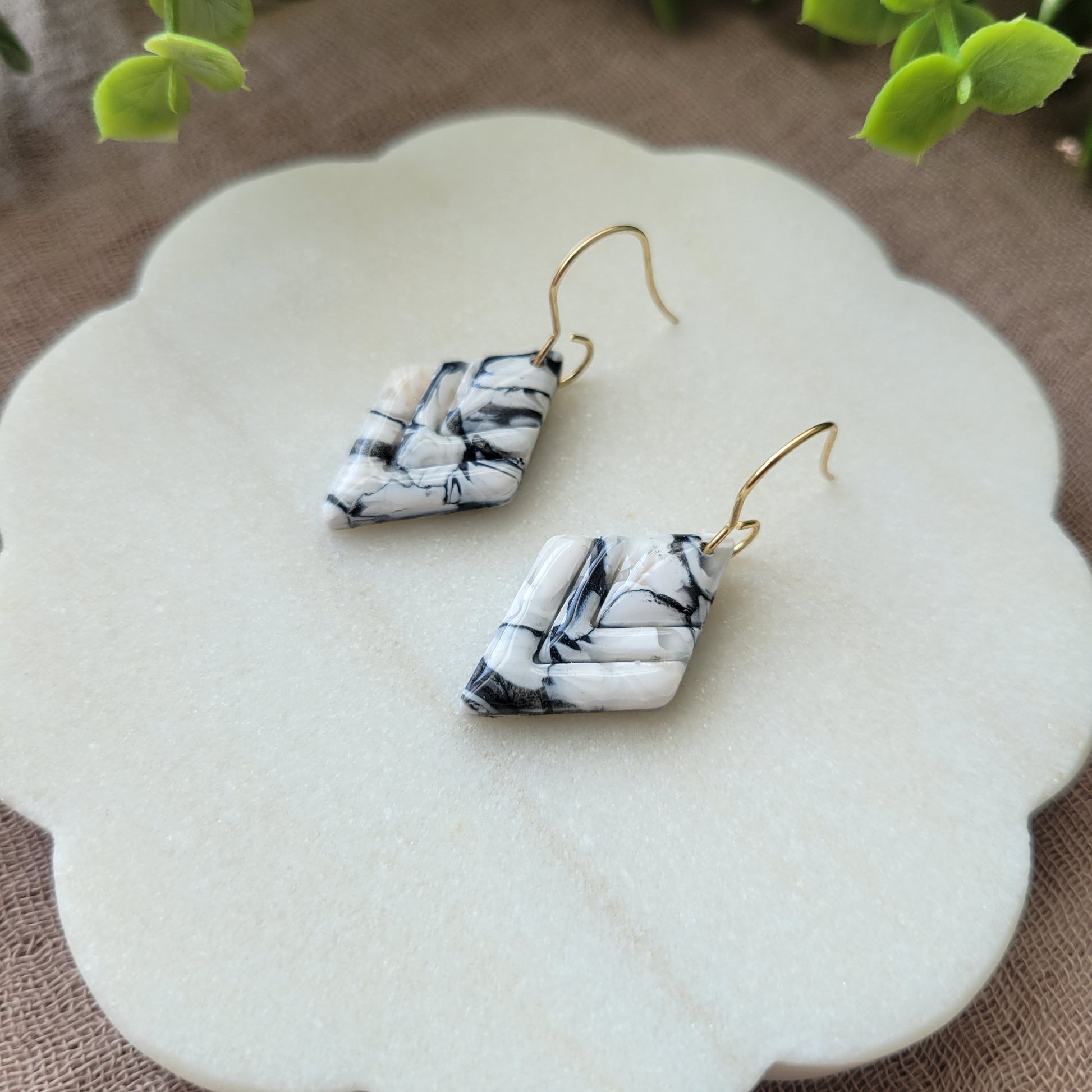 Close up side view of a pair of black, white marble embossed diamond earrings displayed on a white round scalloped tray.