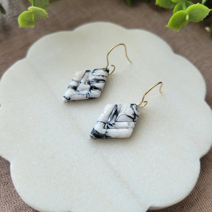 Close up side view of a pair of black, white marble embossed diamond earrings displayed on a white round scalloped tray.