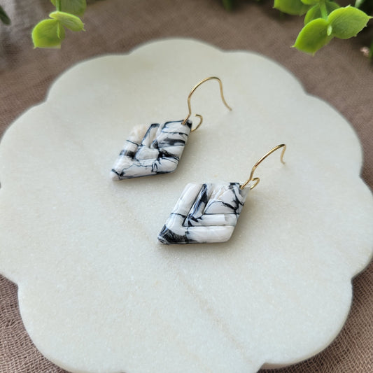 Close up side view of a pair of black, white marble embossed diamond earrings displayed on a white round scalloped tray.