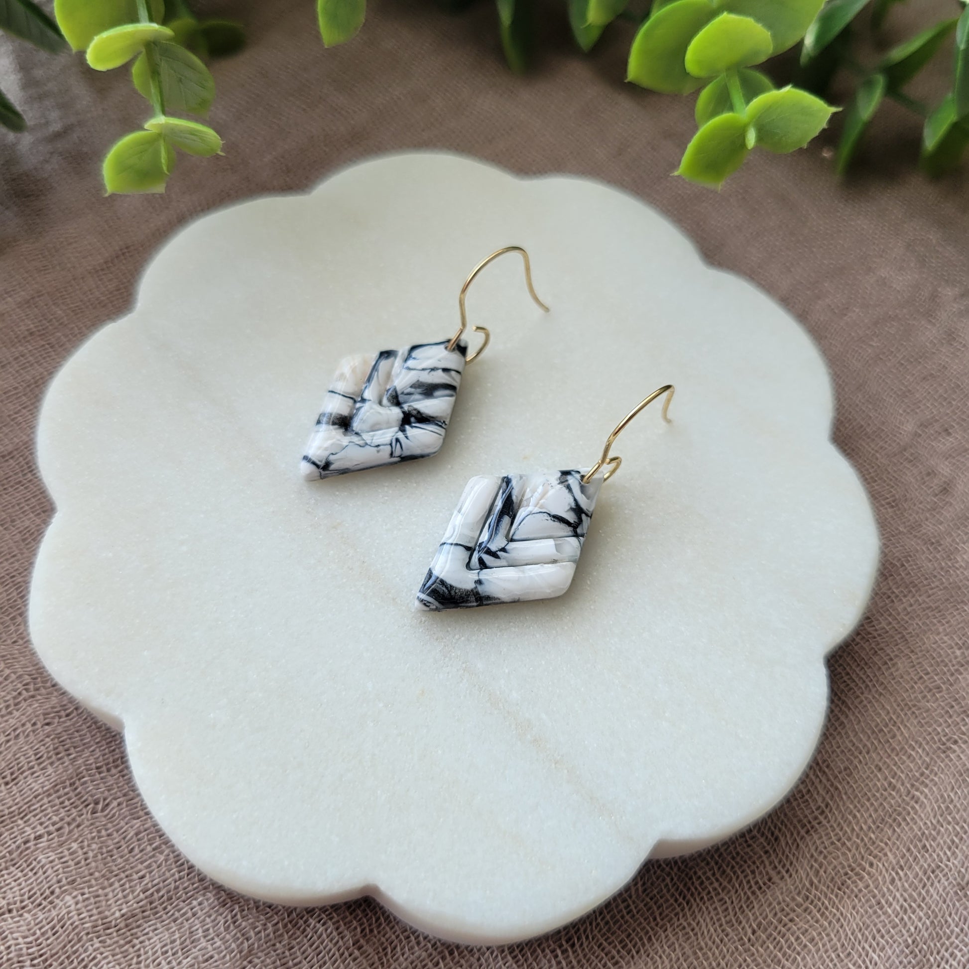 Right side view of a pair of black, white marble embossed diamond earrings displayed on a white round scalloped tray.