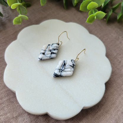Right side view of a pair of black, white marble embossed diamond earrings displayed on a white round scalloped tray.