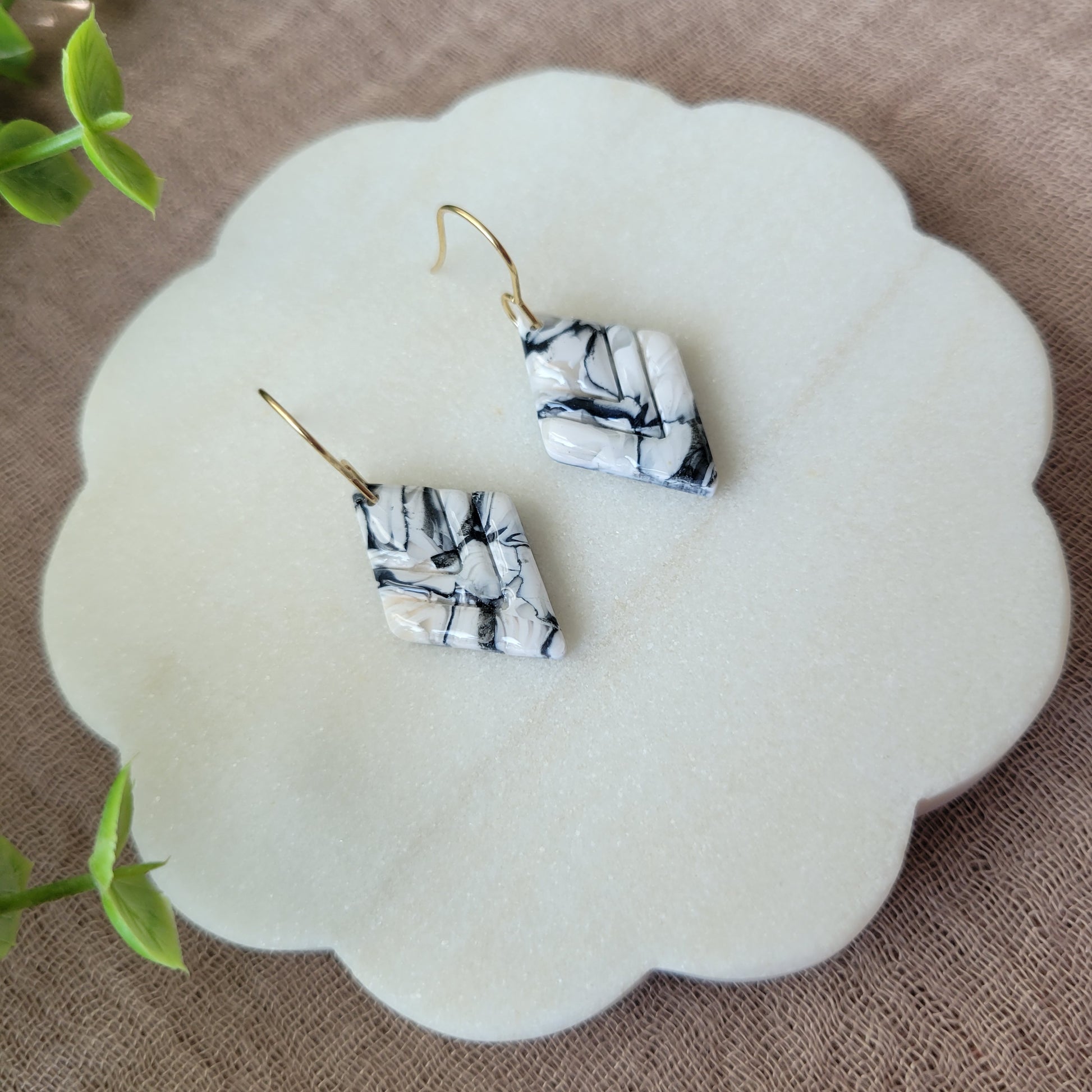 Left side view of a pair of black, white marble embossed diamond earrings displayed on a white round scalloped tray.