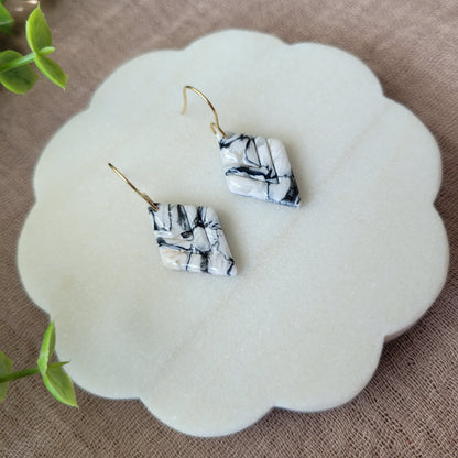 Left side view of a pair of black, white marble embossed diamond earrings displayed on a white round scalloped tray.