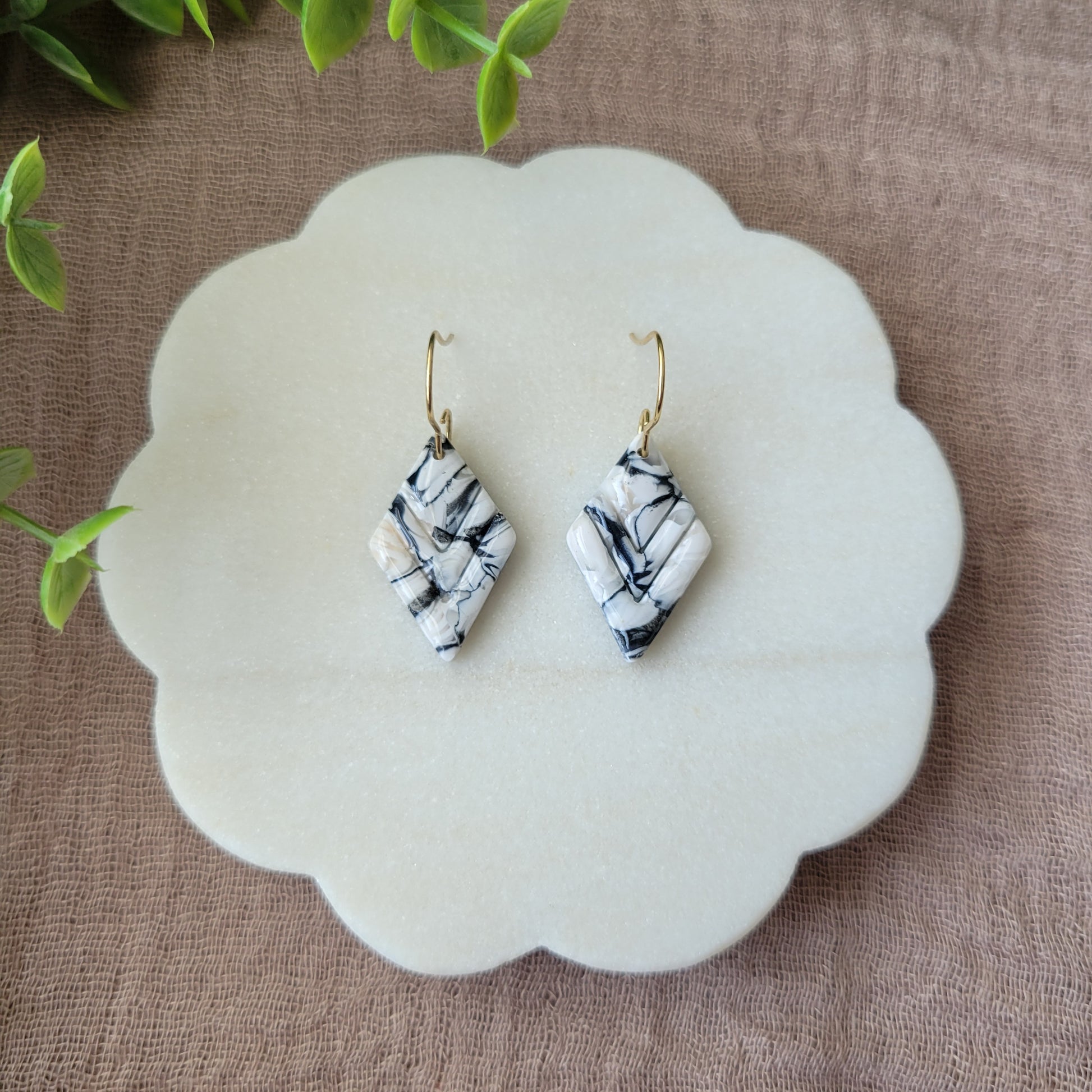 Top view of a pair of black, white marble embossed diamond earrings displayed on a white round scalloped tray.