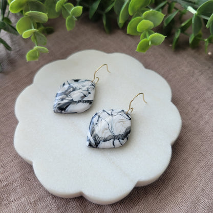 Right side view of a pair of black, white marble round diamond shaped earrings displayed on a white round scalloped tray.
