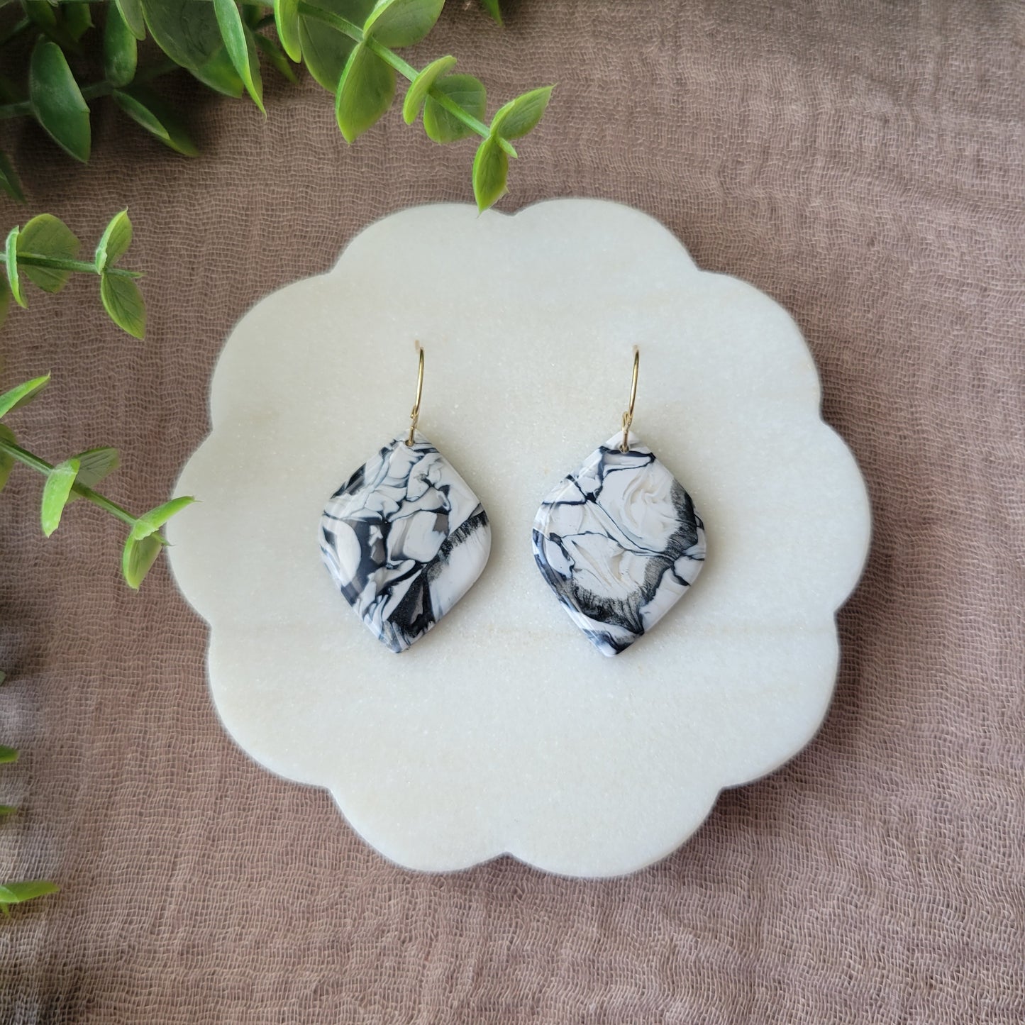 Top view of a pair of black, white marble round diamond shaped earrings displayed on a white round scalloped tray.