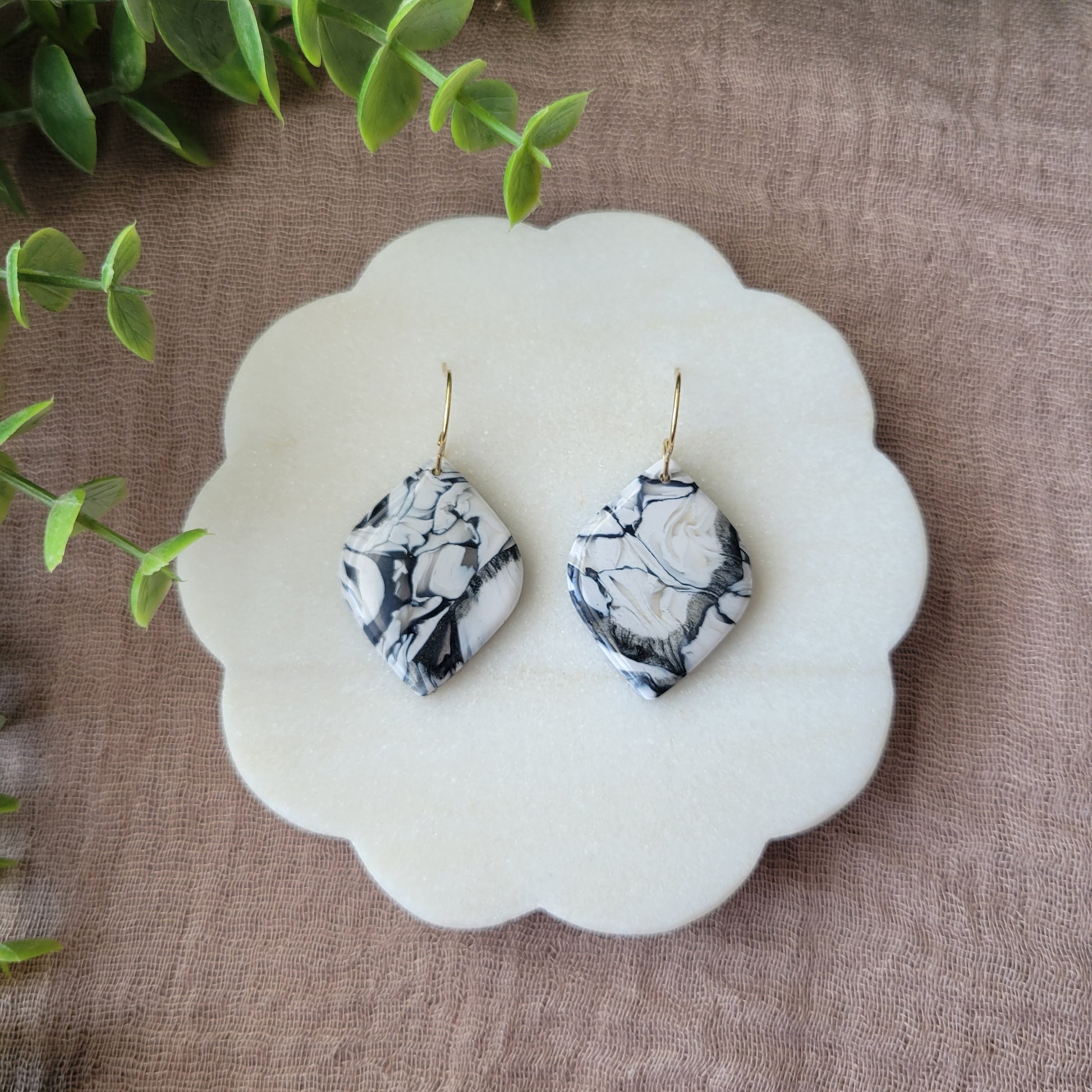 Top view of a pair of black, white marble round diamond shaped earrings displayed on a white round scalloped tray.