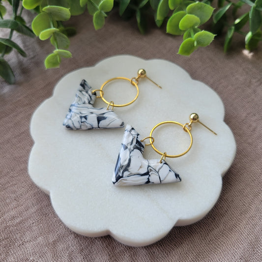 Right side view of a pair of black, white marbled chevron shaped earrings with a gold circle bezel displayed on a white round scalloped tray.