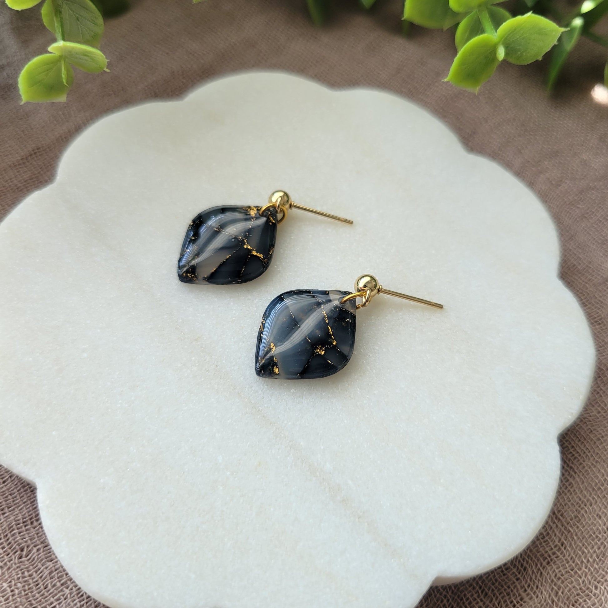 Right side view of a pair of dark blue marble diamond shaped earrings displayed on a white round scalloped tray.