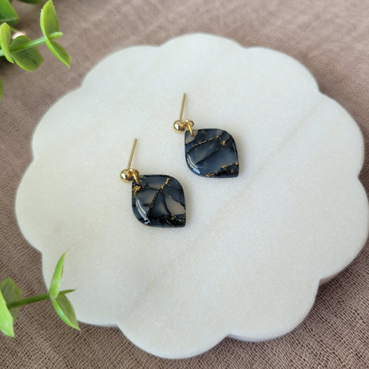 Left side view of a pair of dark blue marble diamond shaped earrings displayed on a white round scalloped tray.