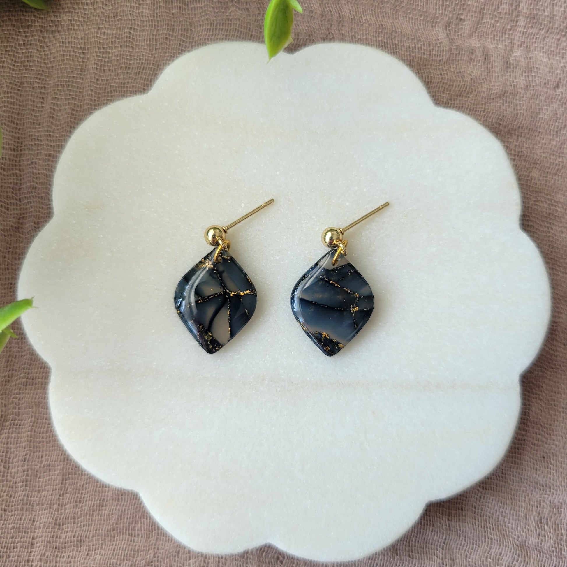 Top view of a pair of dark blue marble diamond shaped earrings displayed on a white round scalloped tray.