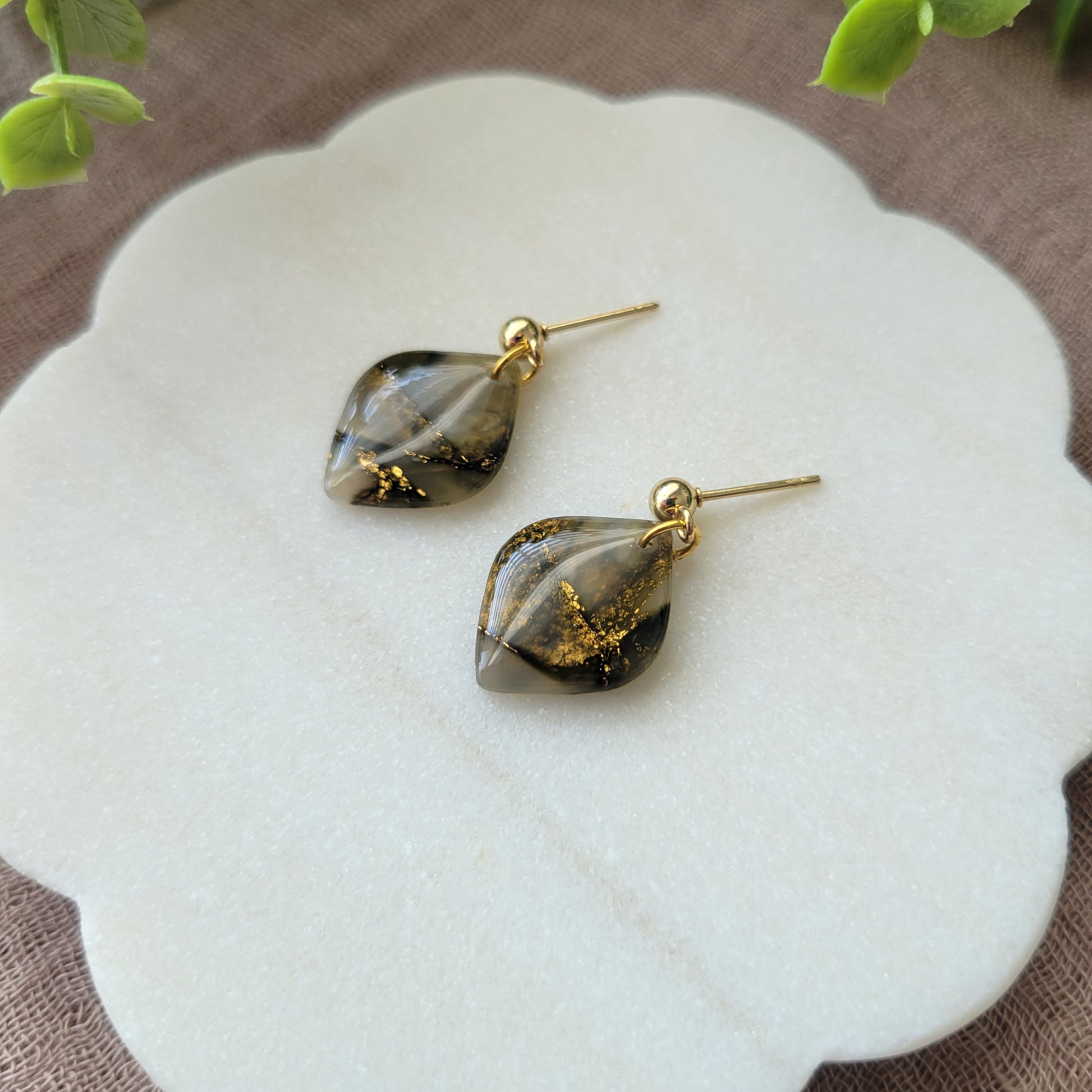 Right side view of a pair of moss green marble diamond shaped earrings displayed on a white round scalloped tray.