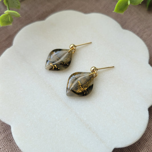 Right side view of a pair of moss green marble diamond shaped earrings displayed on a white round scalloped tray.