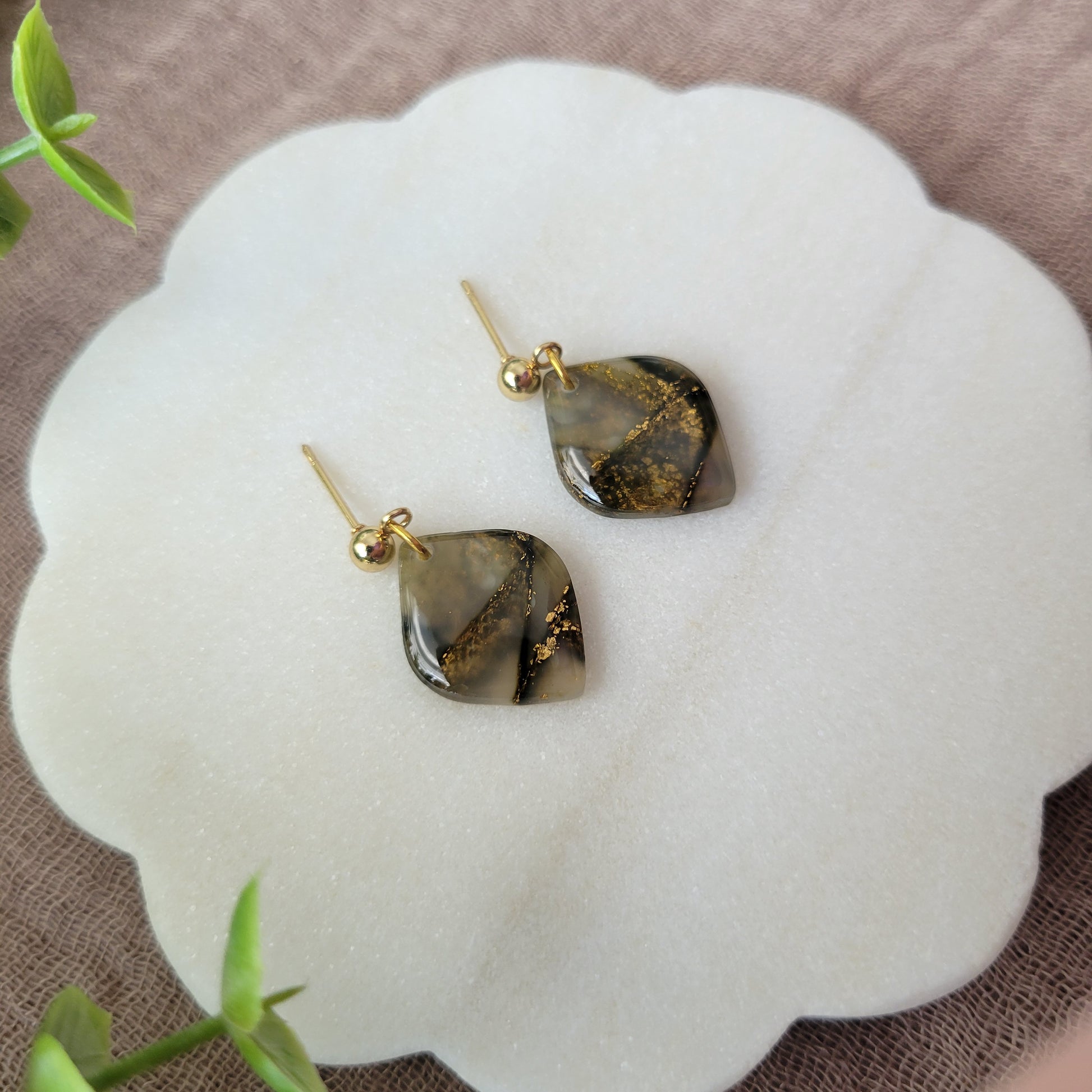 Left side view of a pair of moss green marble diamond shaped earrings displayed on a white round scalloped tray.