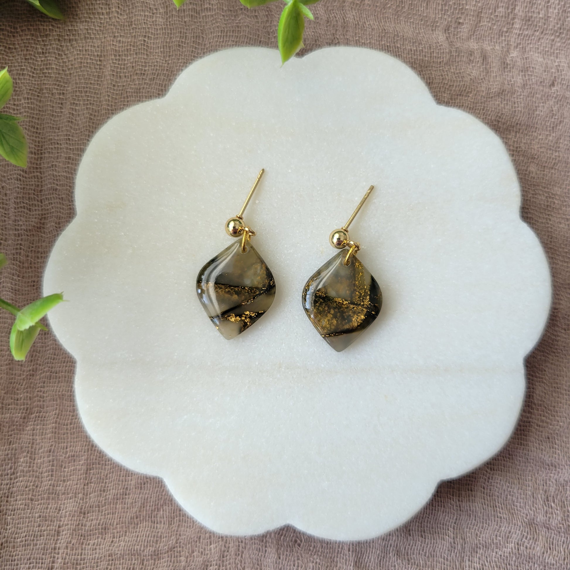 Top view of a pair of moss green marble diamond shaped earrings displayed on a white round scalloped tray.